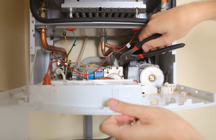 Technician using pliers to repair internal copper pipes and components of a gas boiler.